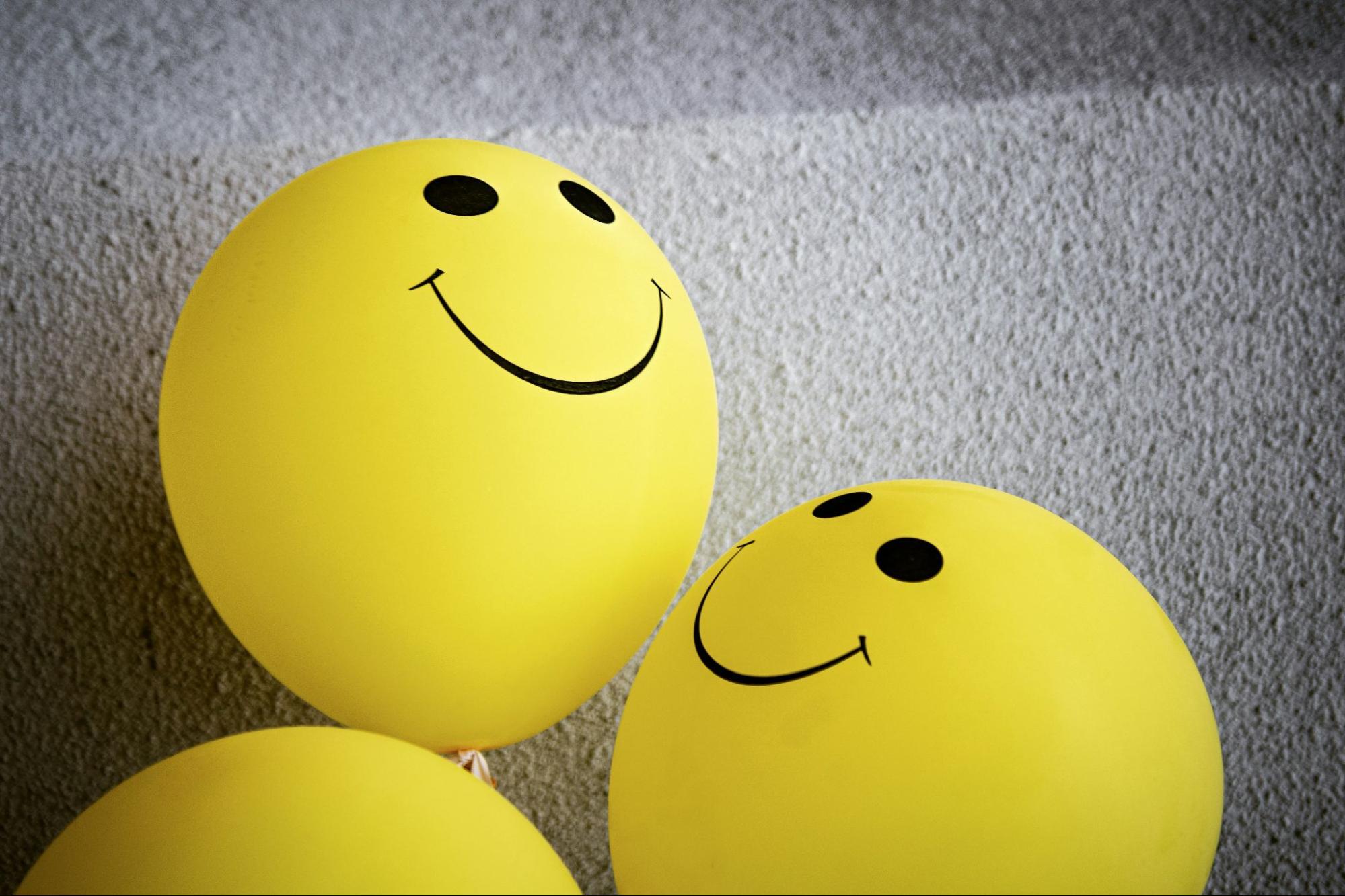 Des ballons de baudruche jaunes sur lesquels sont dessinés des emoticones souriants sont posés sur le sol.