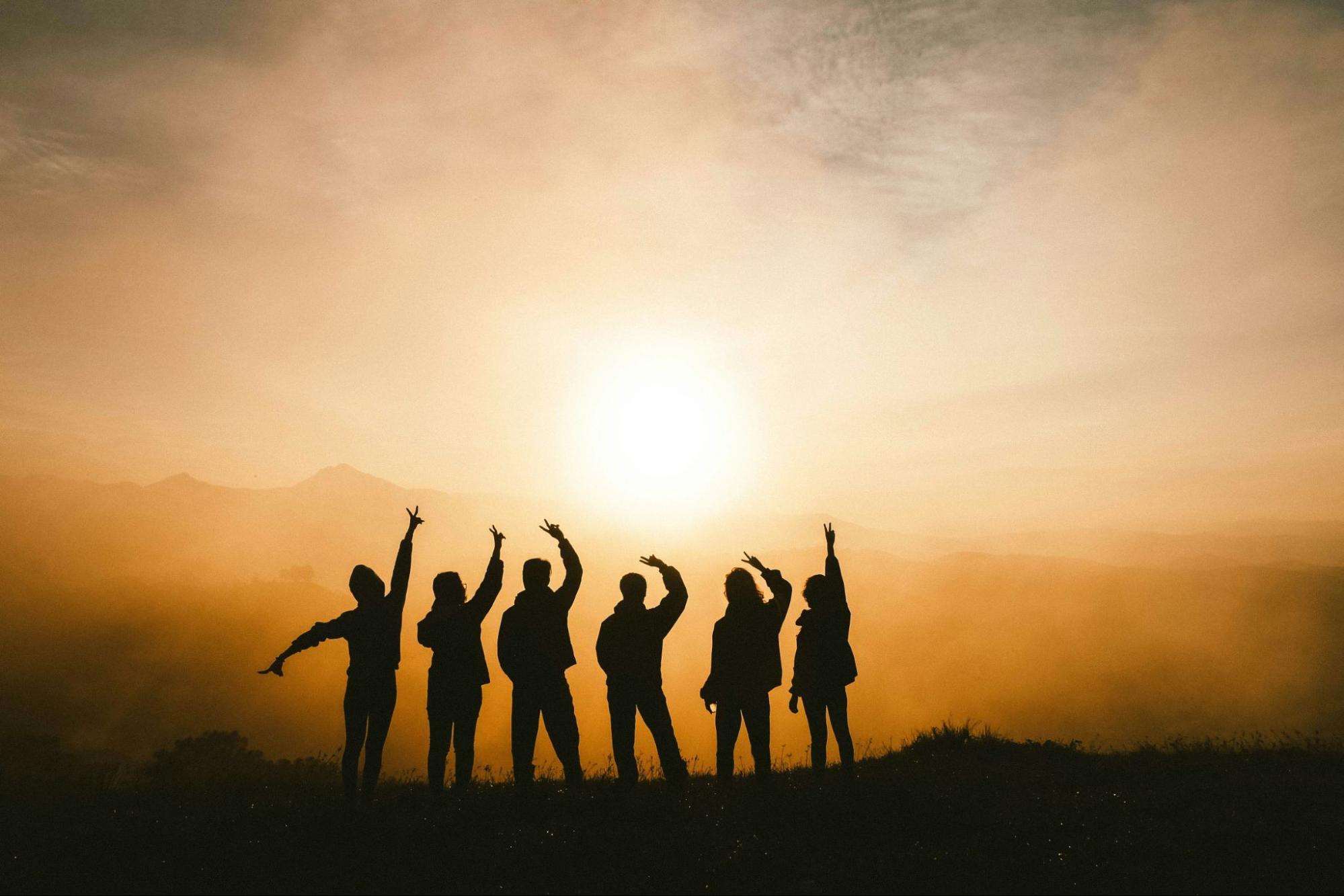 Six silhouettes forment une équipe et lèvent leur bras en signe de joie ils sont face au soleil.